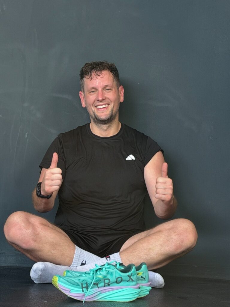 Alex sitzt im Schneidersitz vor einer grauen Wand, trägt die türkisen PUMA-Schuhe und hält beide Daumen hoch, eigenes Foto