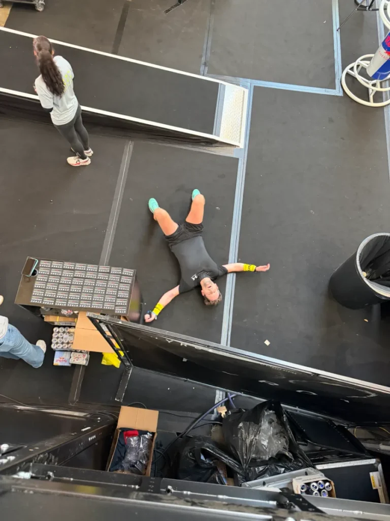 Alex liegt nach dem Rennen bei HYROX Karlsruhe 2026 erschöpft auf dem Hallenboden, von oben fotografiert