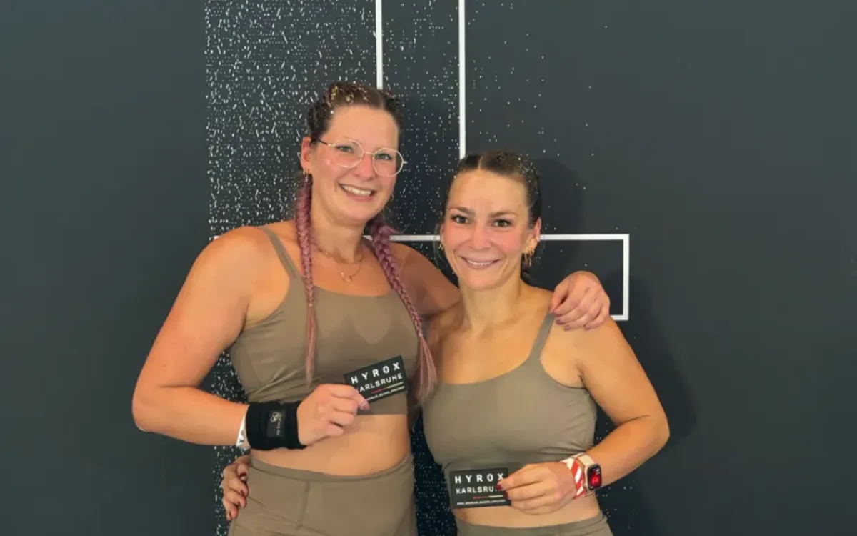 Geri und ihre Doubles-Partnerin halten nach dem Rennen bei HYROX Karlsruhe 2026 ihre Finisher-Patches in die Kamera